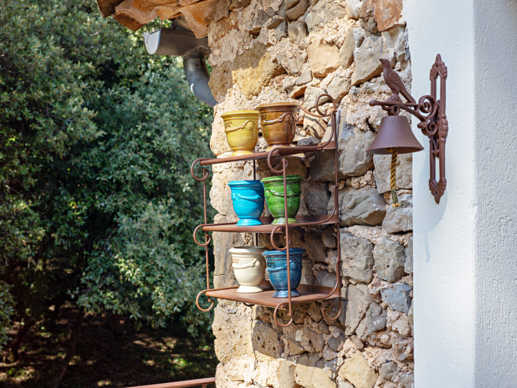 &Eacute;tag&egrave;re en fer forg&eacute; avec pots en c&eacute;ramique color&eacute;s accroch&eacute;e &agrave; un mur en pierre du Mas La Solarie.