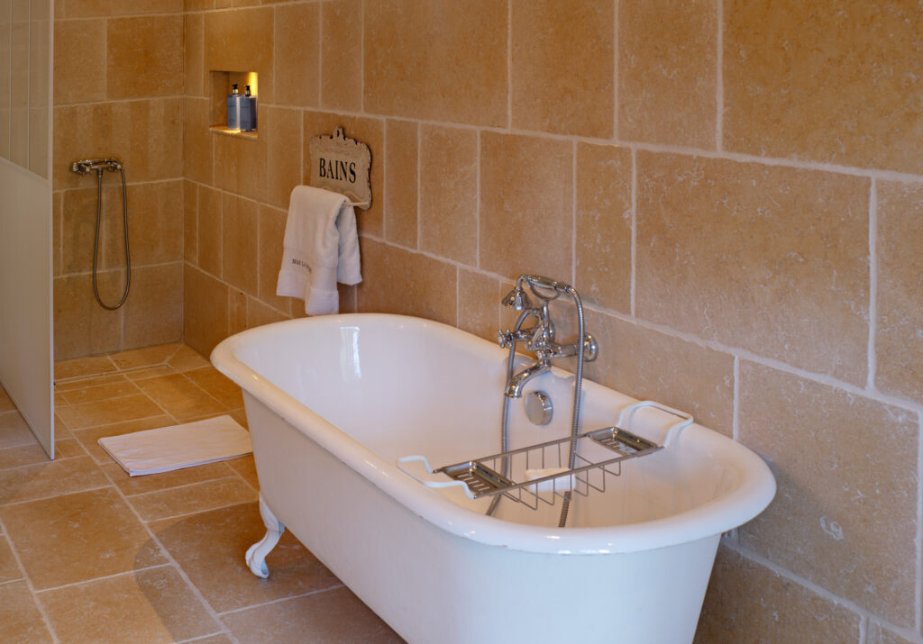 Salle de bain &eacute;l&eacute;gante du Mas La Solarie avec baignoire sur pied, robinetterie chrom&eacute;e et murs en pierre naturelle.