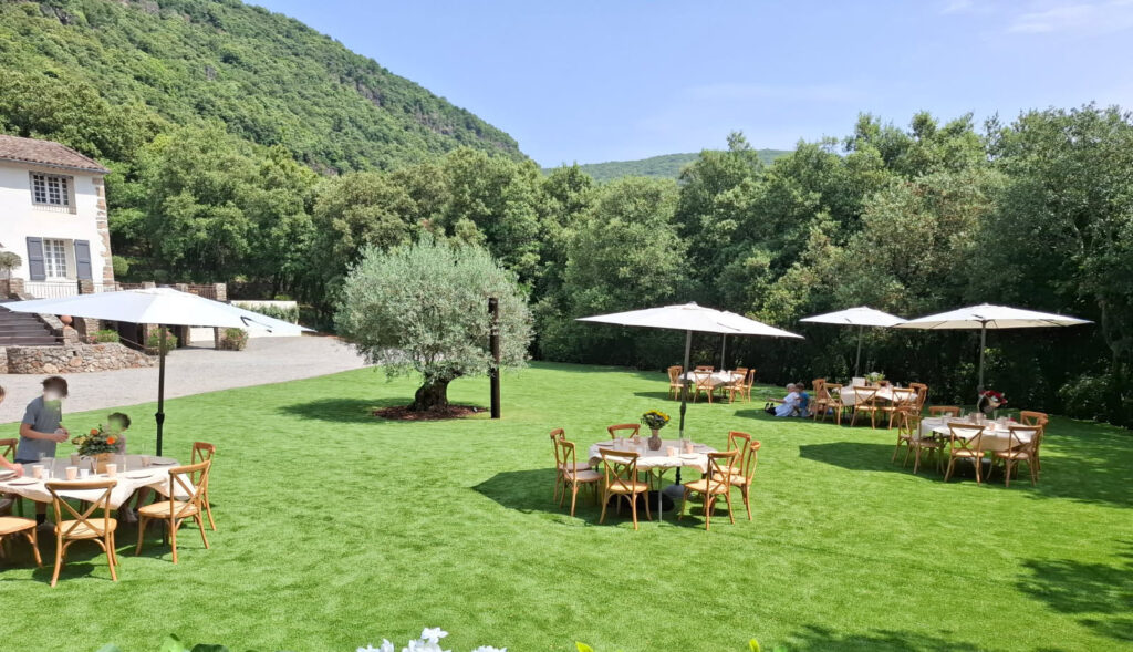 R&eacute;ception en ext&eacute;rieur au Mas La Solarie avec tables rondes, parasols et olivier, lieu de mariage dans les C&eacute;vennes