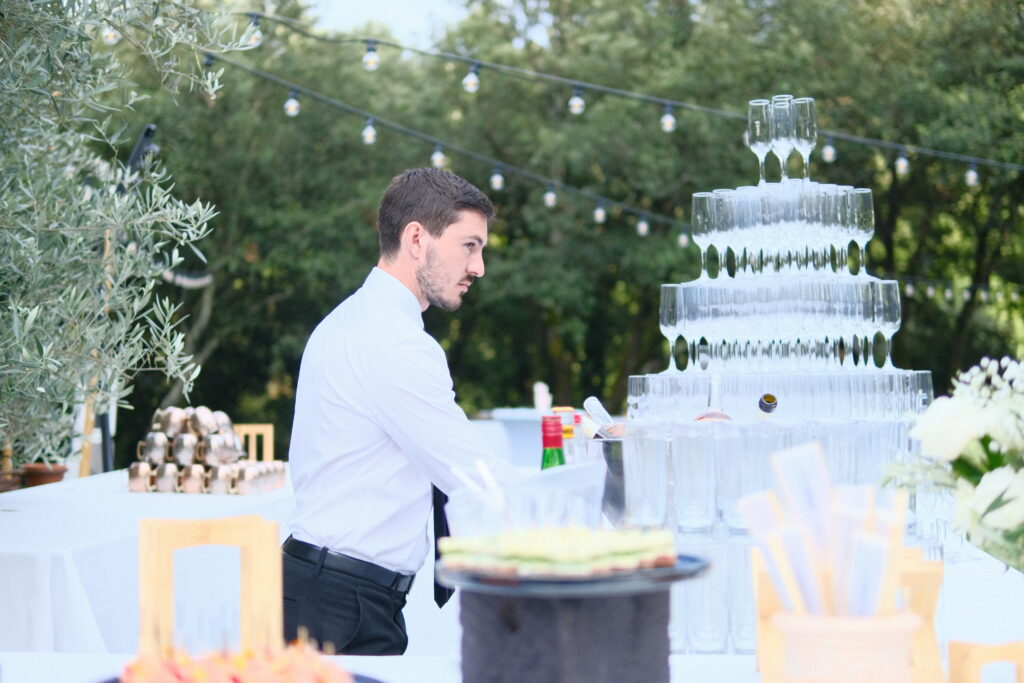 Serveur en costume pr&eacute;parant une pyramide de verres pour un mariage au Mas La Solarie, lieu de r&eacute;ception raffin&eacute; dans les C&eacute;vennes.
