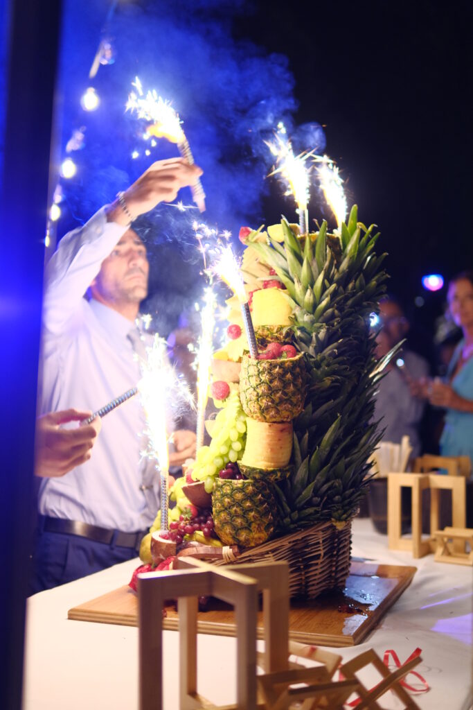 Buffet de fruits d&eacute;coratif avec ananas, raisins et fruits exotiques, orn&eacute; de cierges scintillants lors d&rsquo;une r&eacute;ception de mariage au Mas La Solarie dans les C&eacute;vennes.